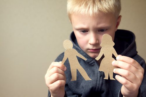 Child holding cardboard cutout figures, looking pensive.