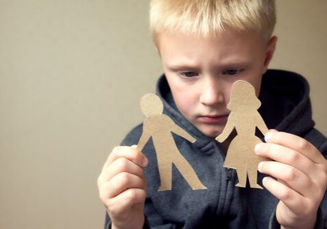 Child holding cardboard cutout figures, looking pensive.