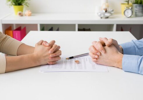 Hands folded over divorce papers on table.